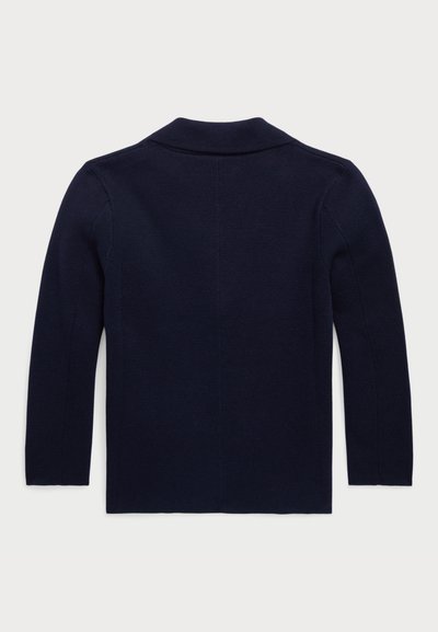 Tumši zilas krāsas adīta džemperis ar šaulu apkakli, garām piedurknēm un gludu faktūru. Aizmugurējā daļa ir vienkārša, ar minimālām dizaina detaļām.