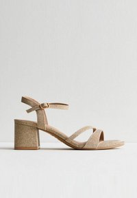 Sandali con tacco a blocco dorati glitterati, caratterizzati da più bande, una fibbia alla caviglia e un design open toe. Suola liscia e tacco robusto.