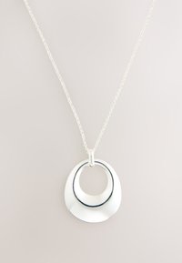 Silver pendant necklace featuring two smooth, overlapping hollow crescent shapes on a delicate chain against a neutral background.