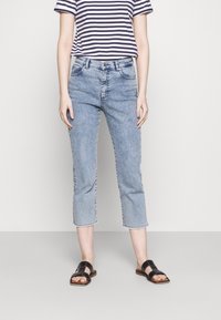 Jeans de tiro bajo y lavado claro, con pierna recta y dobladillo desgastado, combinados con una camiseta a rayas en azul marino y blanco. Sandalias negras con suela plana.