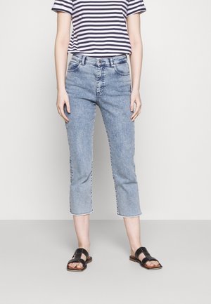 Jean délavé, cropped, avec une jambe droite et un ourlet effiloché, associé à un T-shirt rayé bleu marine et blanc. Sandales noires à semelle plate.