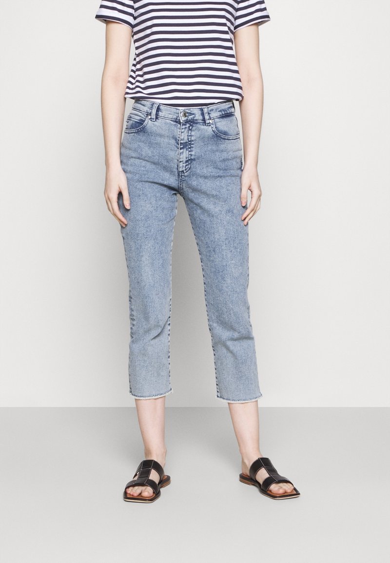 Jeans de tiro bajo y lavado claro, con pierna recta y dobladillo desgastado, combinados con una camiseta a rayas en azul marino y blanco. Sandalias negras con suela plana.