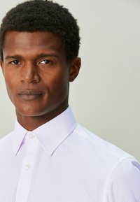 Hellviolettes gestreiftes Hemd mit Standardkragen, vorne mit Knöpfen zu schließen und glatter Textur. Das Modell hat eine kurz geschnittene Frisur.