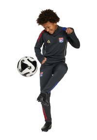 Ensemble de survêtement gris foncé avec des accents rouges et bleus, veste zippée et pantalon ajusté. Ballon de football noir et chaussures à crampons inclus.