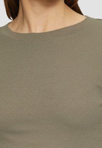 Top acanalado en verde oliva con escote redondo. La tela presenta una textura sutil que enfatiza su diseño ajustado y su acabado suave.