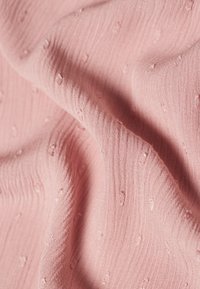 Hellrosa Stoff mit einem strukturierten Muster, das kleine erhabene Punkte und dezente horizontale Linien aufweist und eine weiche, taktile Optik erzeugt.