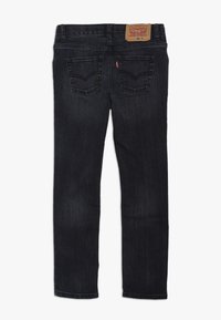 Jeans de mezclilla de lavado oscuro con un diseño de pierna recta, estilo de cinco bolsillos, costuras reforzadas y una etiqueta de marca de cuero visible en la parte posterior.