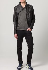 Męska czarna skórzana kurtka o fakturowanym wykończeniu, szara koszulka, czarne jeansy oraz niebieskie trampki z zielonymi akcentami. Casualowy strój.