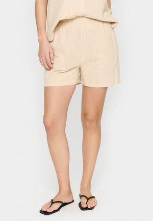 Beige shorts met een elastische tailleband, gemaakt van een lichtgewicht stof, met een subtiele geribbelde textuur, gecombineerd met zwarte slippers.