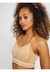 Beige sport-bh tillverkad av stretchigt material med en ribbad band, samlad frontdetalj, tunna justerbara band och Hummel-logga i accent.