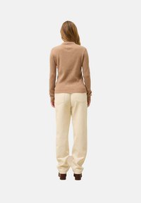 Ribbeliger brauner Pullover kombiniert mit cremefarbenen Hosen, die einen lockeren Schnitt und gerade Beine haben, getragen mit dunkelbraunen Absatzstiefeln.