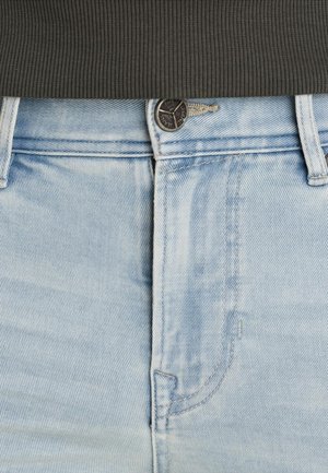 Hellblaue Jeans aus Denim mit sichtbarer Knopfleiste und vorderen Taschen, kombiniert mit einem dunklen gerippten Pulloverbund.