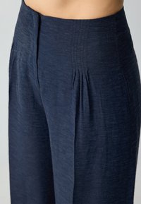 Marineblauwe wijde broek heeft een gestructureerde stof, geplooide taille en zijzakken, ontworpen met een ontspannen silhouet.