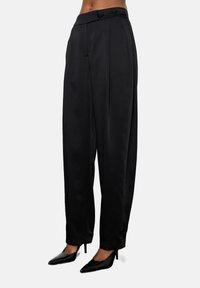 Fekete selyem széles lábú nadrág magas derekú fazonban, gombos részletekkel és sima textúrával. Fekete, hegyes orrú magassarkúval párosítva.