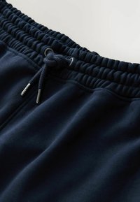 Navyblaue Sweatpants mit elastischem Bund, Kordelzugverschluss und glatter Textur. Mit metallischen Akzenten an den Enden des Kordelzugs.