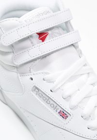 Witte hoge sneakers van leer, voorzien van klittenbandsluitingen, gestructureerde zijkanten en een rood en zilver logo.