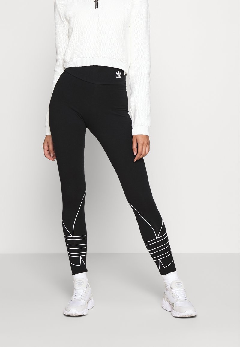 Svarta leggings med vita accentlinjer och mönster, hög midja, kombinerat med en texturerad vit kortärmad tröja och vita sneakers.
