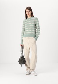 Lichtgroen gebreid sweater met crème hartpatronen, geribde manchetten en zoom; gecombineerd met off-white cargobroeken en een grijze tas.