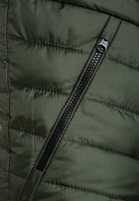 Quilted green puffer jacket material with a black zipper detail. The fabric has a smooth texture and distinct horizontal stitching pattern.