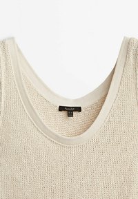 Débardeur en maille couleur crème avec un col rond et une étiquette de marque noire à l'intérieur du col.