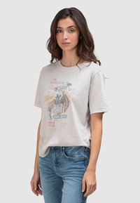 Roomkleurig katoenen T-shirt met korte mouwen, voorzien van een vintage rodeo grafische print in rood, blauw en geel. Gecombineerd met een blauwe spijkerbroek.