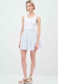Top bianco senza maniche con borchie argentate, abbinato a una gonna plissettata a righe blu chiaro e bianca. Presenta sandali piatti beige con fibbia.