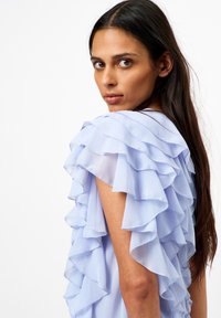 Lichtblauwe jurk met gelaagde ruches op de schouders. Zachte stof, vloeiende ontwerp en subtiele textuur verbeteren de algehele uitstraling.