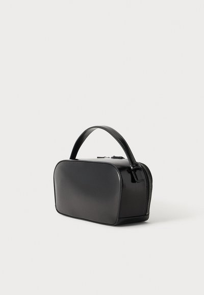 Petit sac à main rectangulaire noir aux bords arrondis, avec une seule poignée supérieure et une fermeture éclair latérale sur un fond clair uni.