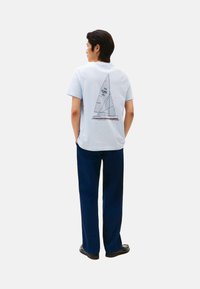 Camiseta de algodón de color azul claro con un gráfico geométrico de un velero en líneas oscuras en la parte posterior. Combinada con pantalones de color azul marino.