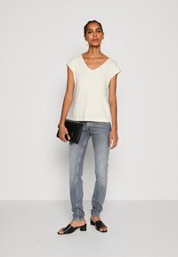 Creme v-hals t-shirt, lichtblauwe skinny jeans, zwarte open-toe mules en een zwarte clutch. Soepele stof en een relaxte fit.