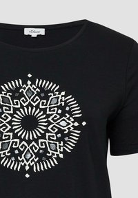 Zwarte T-shirt met een ronde hals en een wit en metallic zilveren cirkelvormig mandala ontwerp in het midden. Korte mouwen.