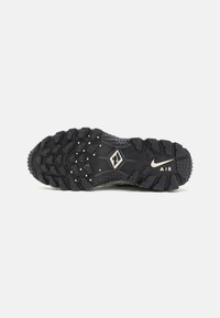 Black athletic shoe sole features rugged treads, textured surface, and prominent branding. Durable rubber with small studs for traction.