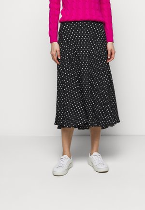 Jupe midi noire à pois blancs, confectionnée dans un tissu léger, avec une coupe évasée. Associée à des baskets blanches.