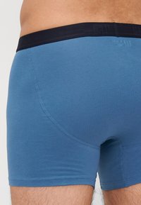 Kék pamut keverék boxer nadrág fekete derékkal, amelyen a márka logója található, sima textúrával és testhez álló fazonnal.