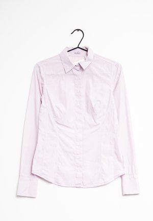 Jasnoróżowa, długorękawowa koszula na guziki z kołnierzem, wisząca na czarnym wieszaku na białym tle.