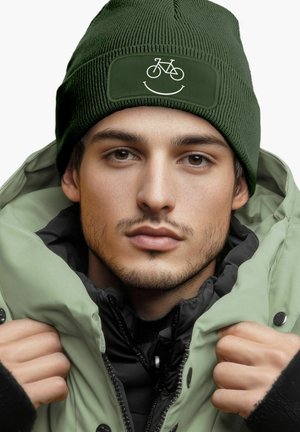 Green knit beanie with a bicycle and smile graphic on the front, worn with a light green and black insulated jacket. Textured fabric.