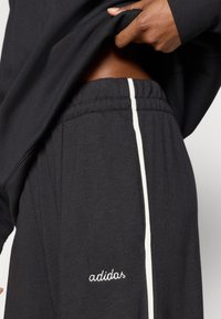 Crne trenirka hlače s bijelom bočnom prugom i izvezenim logotipom "adidas". Mekani materijal, elastični pojas, ležerni kroj.