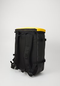 Zaino nero con parte superiore gialla, realizzato in materiale resistente. Dotato di spallacci regolabili, cerniere e cuciture rinforzate.