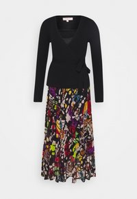 Haut cache-cœur noir côtelé à manches longues, associé à une jupe fluide à motifs floraux multicolores. La jupe présente des teintes vibrantes et des formes abstraites.