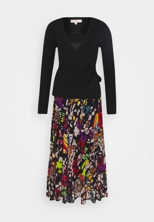 Černý žebrovaný zavinovací top s dlouhými rukávy, doplněný volnou vícbarevnou sukní s květinovým vzorem. Sukně se vyznačuje živými odstíny a abstraktními tvary.