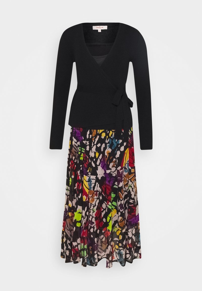 Haut cache-cœur noir côtelé à manches longues, associé à une jupe fluide à motifs floraux multicolores. La jupe présente des teintes vibrantes et des formes abstraites.