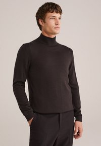 Pulover cu guler înalt de culoare maro închis, cu un design ajustat, fabricat dintr-un material moale, cu mansete ribbate și detalii subtile pe umeri.