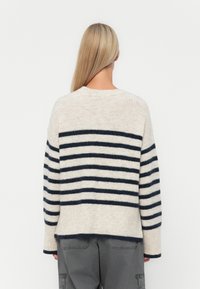Neulepusero, jossa on vaaleanbeige kangas ja tummansinisiä vaakaraitoja, pyöreä pääntie ja laskeutuvat olkapäät, päättyen lantiolle.