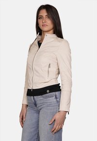 Giacca di pelle cream con colletto rialzato, chiusura a zip sul davanti e due tasche laterali. Silhouette aderente, abbinata a jeans casual.