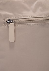 Borsa di tessuto beige con una piccola tasca con zip e un tirante in metallo argentato, caratterizzata da una superficie testurizzata. Cuciture rinforzate lungo i bordi.