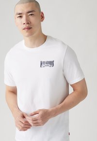 Tricou din bumbac alb cu maneci scurte, având un logo al Levi Strauss & Co. imprimat pe partea stângă a pieptului. Textură netedă.