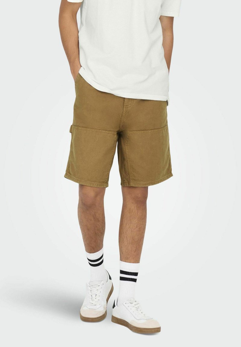 Khaki cargo shorts med fire lommer, lavet af bomuldsstof, med stikninger og en afslappet pasform, parret med hvide sneakers og stribede sokker.