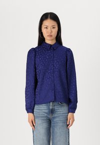 Navy blue button-up shirt with heart pattern, long sleeves, and puffed shoulders. Features a collar and a relaxed fit. Worn with light jeans.