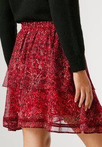 Punainen kuviollinen hame, joka on valmistettu kevyestä kankaasta. Siinä on volanttimuotoilu ja joustava vyötärö. Kerrokset luovat tekstuurisen ilmeen.