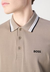 Bežna polo majica z teksturirano tkanino, ki ima trojno gumbno zapiranje, kontrastno črno-bele črtaste ovratnike in vezeno logotip "BOSS".